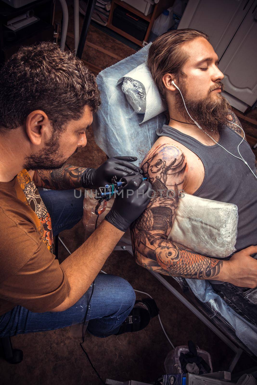 Tattooist makes tattoo pictures in tattoo parlor./Man wearing gloves doing tattoo in salon.