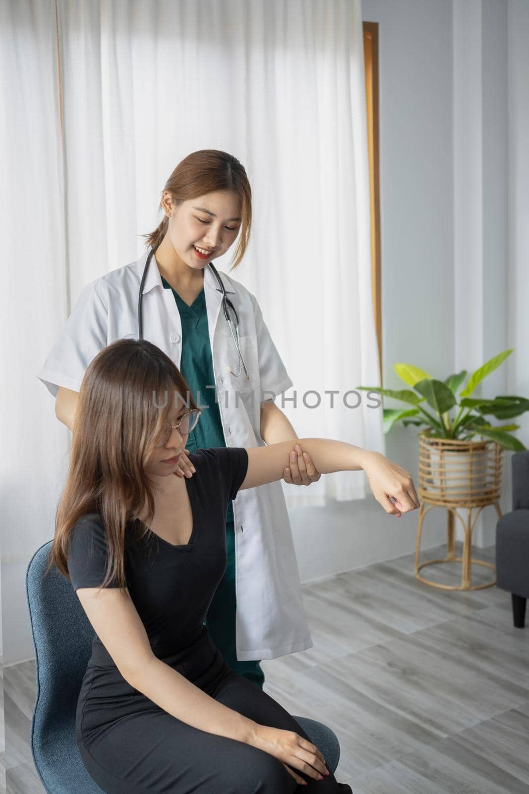 Female physiotherapist working examining treating injured arm of female patient in clinic.