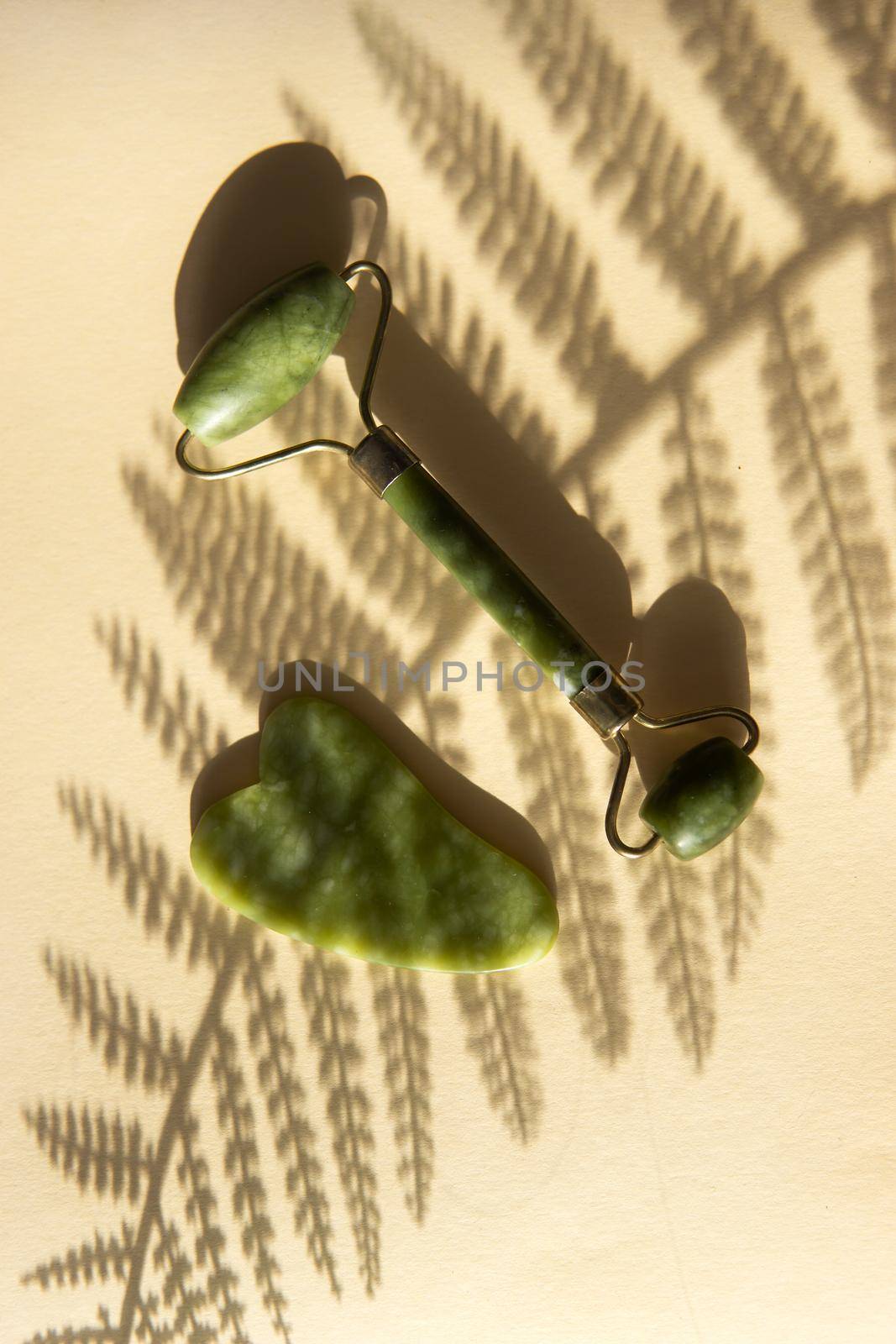 Jade Gua sha scraper and facial massager on beige background. Hard light, shadows, the concept self-care. Facial care. Zero waste. Lifting and toning treatment at home.