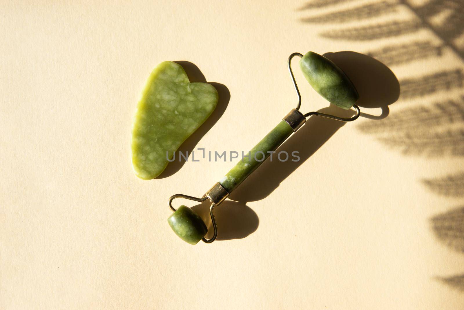 Jade Gua sha scraper and facial massager on beige background. Hard light, shadows, the concept self-care. Facial care. Zero waste. Lifting and toning treatment at home.