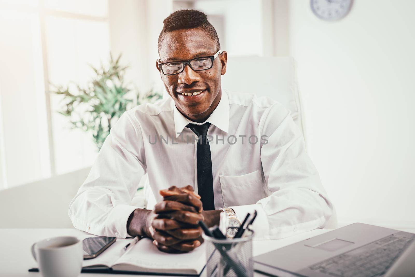 African smiling businessman is sitting in the office satisfied with his work.