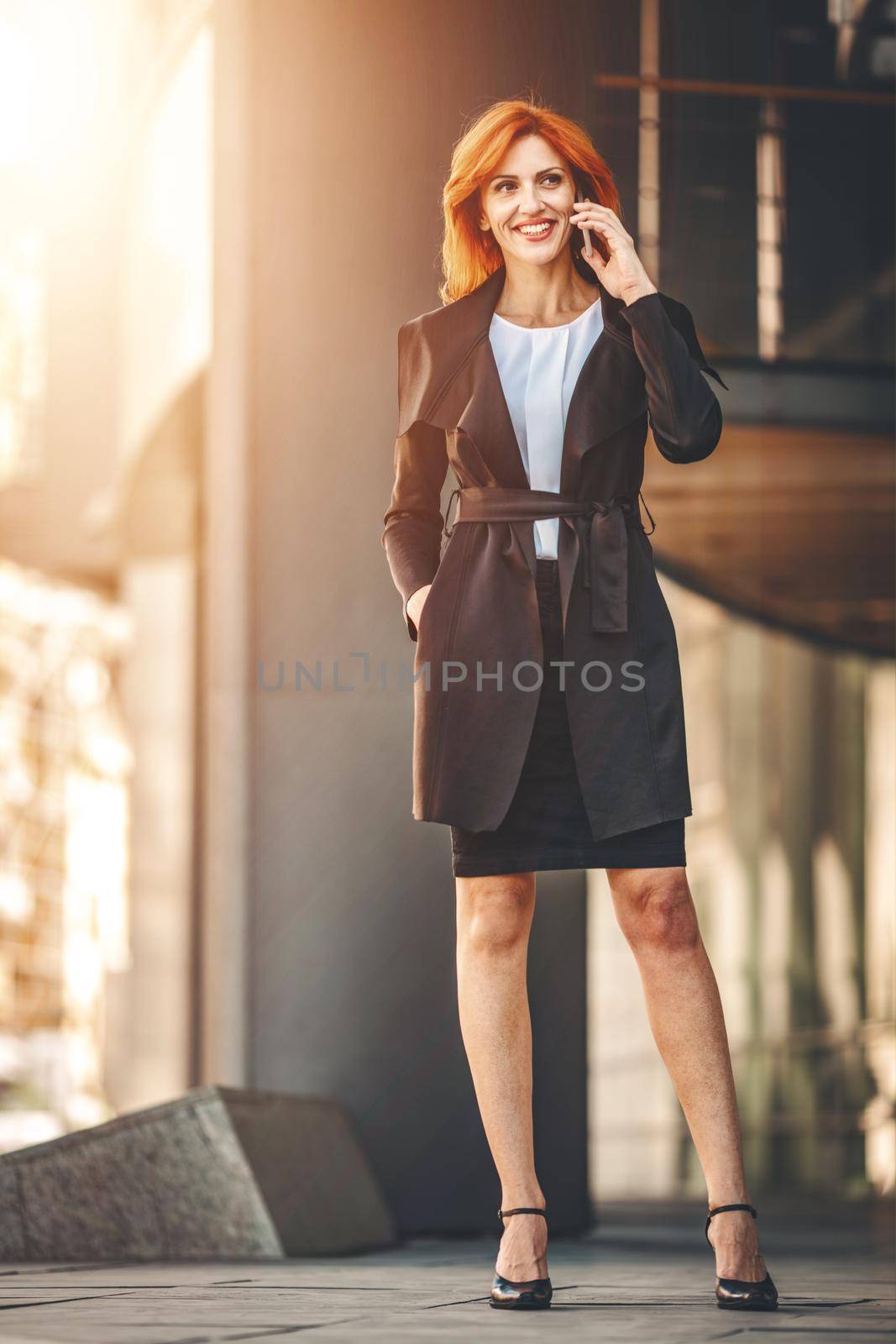 Smiling successful business woman is talking on smartphone in office district.