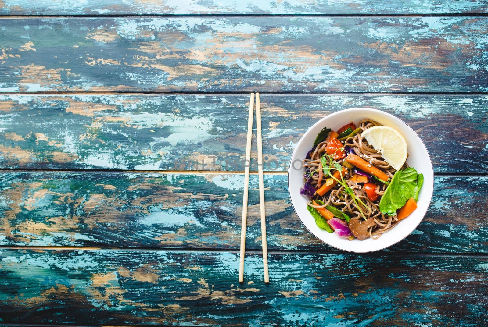 Asian noodles with vegetables, bowl, rustic wooden old background. Space for text. Top view. Soba noodles, vegetables, mushrooms, chopsticks. Vegetarian/Vegan noodles. Asian style dinner with noodles