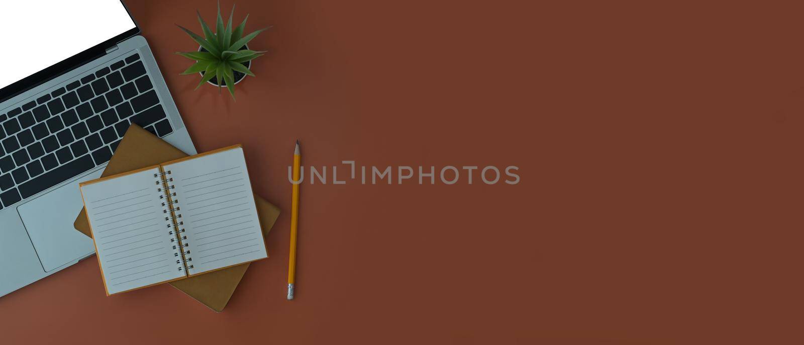 Laptop computer, coffee cup, plant and notebook on brown background with copy space.