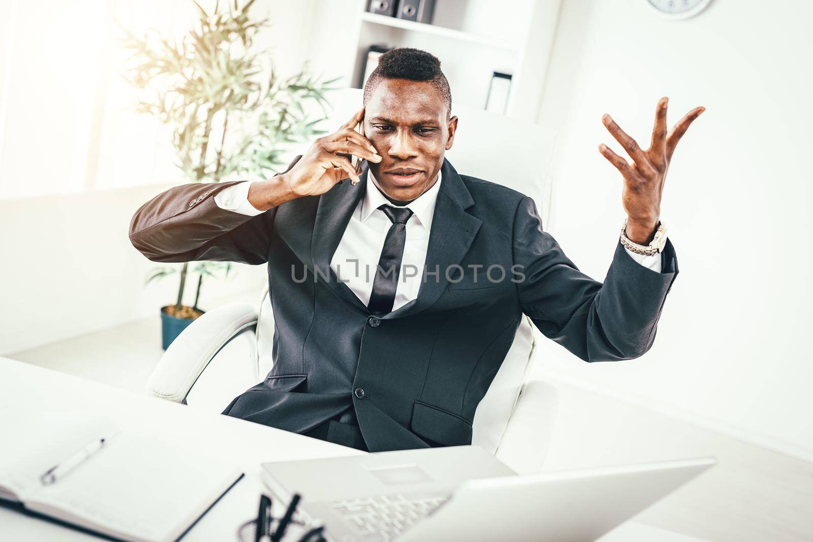 Pensive African businessman talking on smartphone in modern office. 