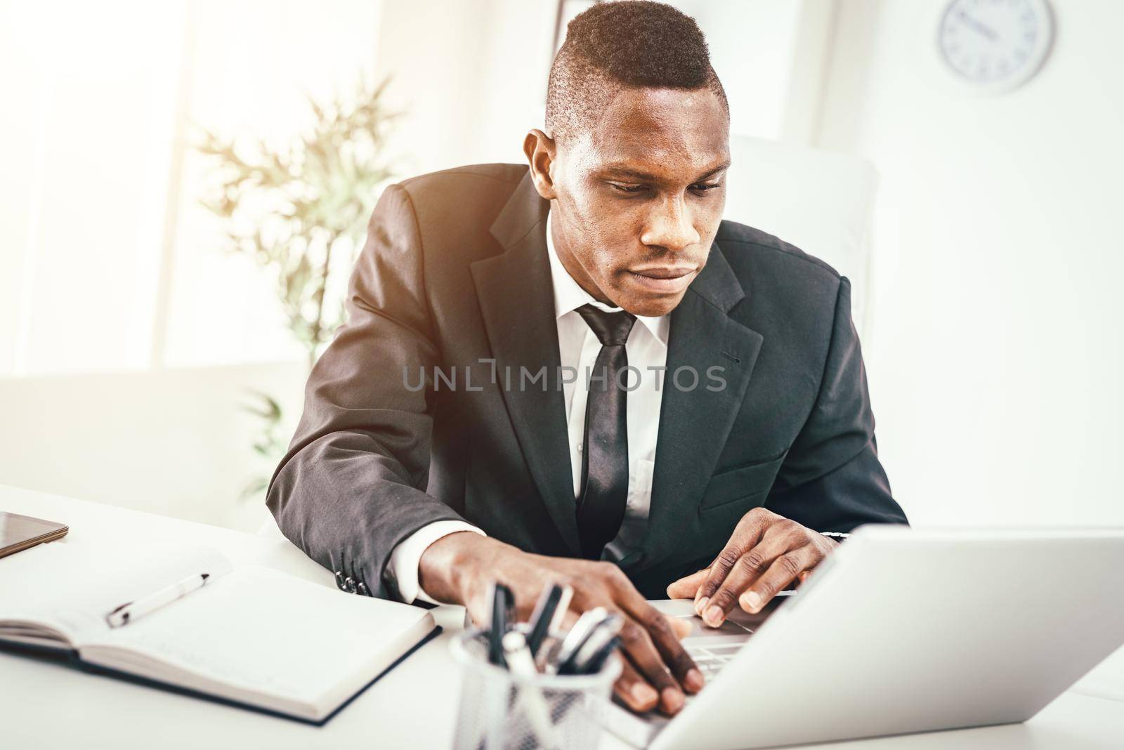 Pensive African businessman working on laptop in modern office.