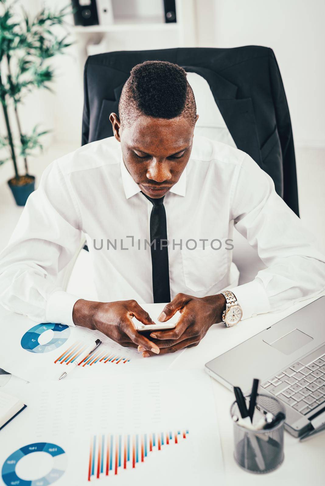 Pensive African businessman working on calculator in modern office and planning what to do next.