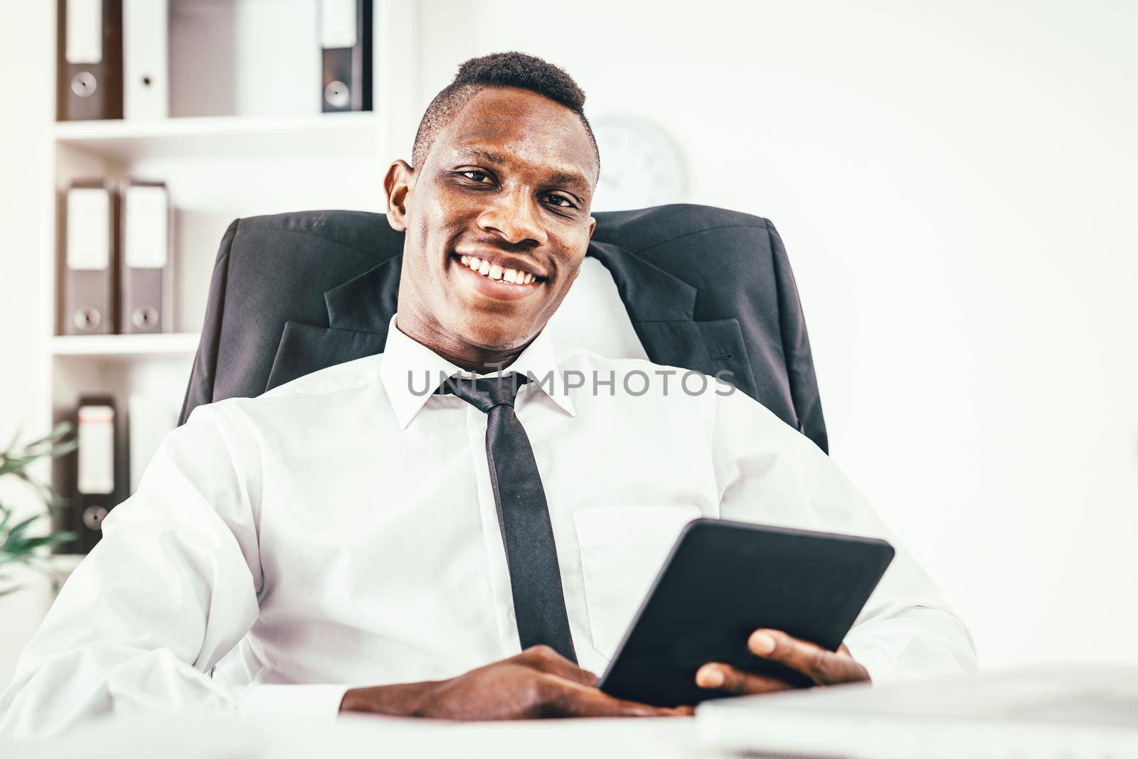 Satisfied African businessman working on digital tablet in modern office.