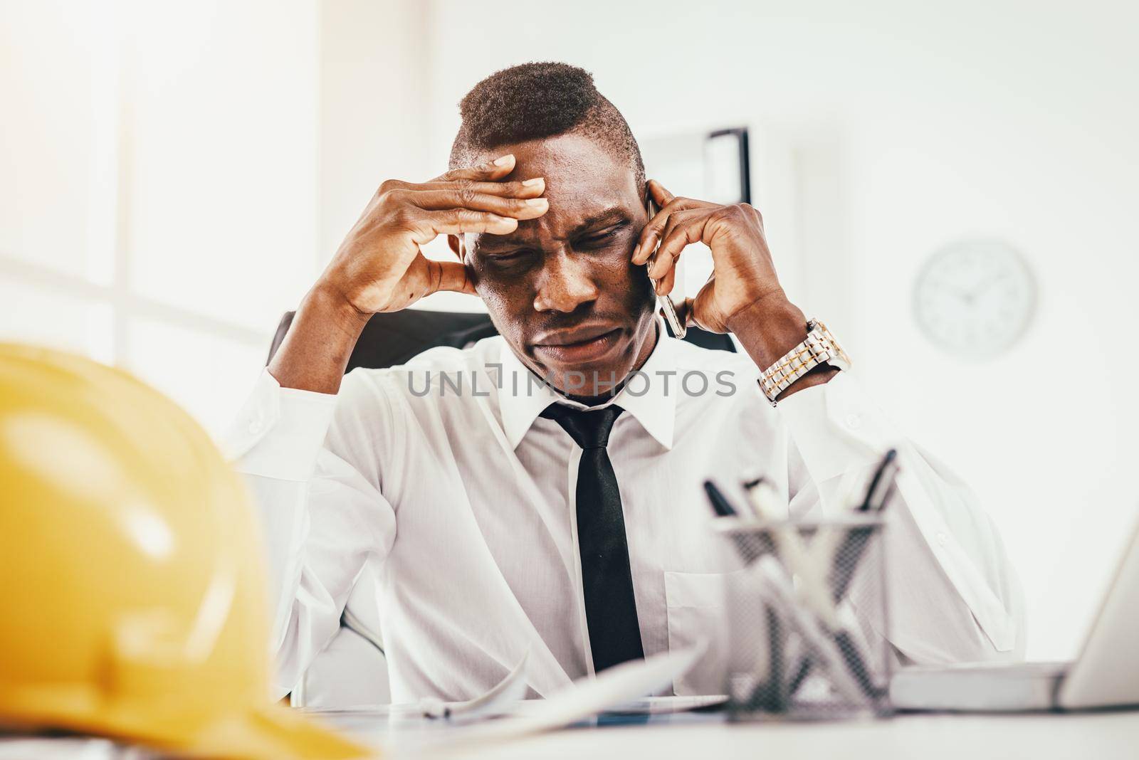 Pensive African businessman talking on smartphone in modern office. 