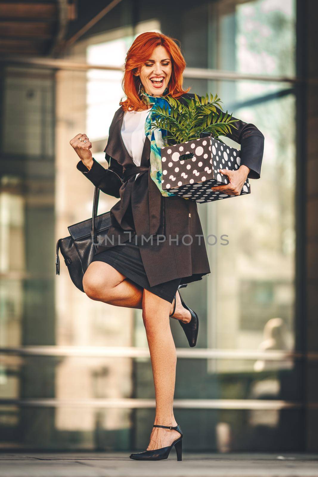 Happy business woman is celebrating success in office district with a box full of her personal belongings from the office just after she gives up job. 