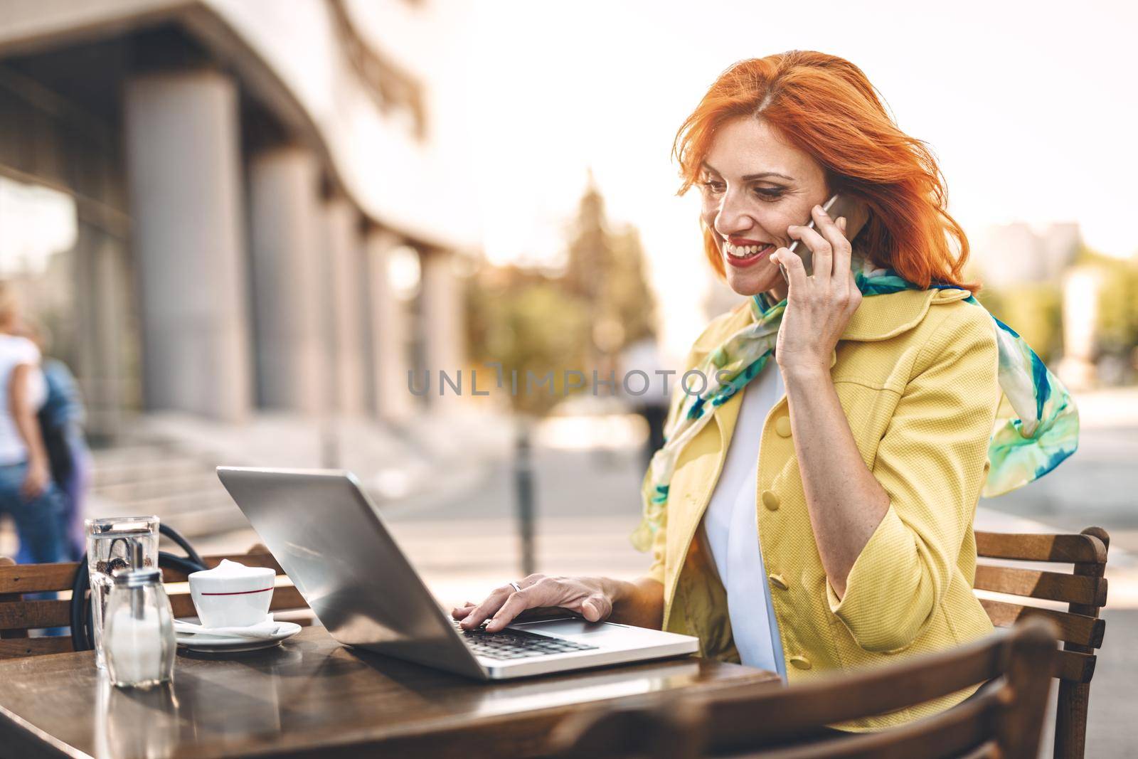 Business woman is working at the laptop and using smartphone on a coffee break in a street cafe.