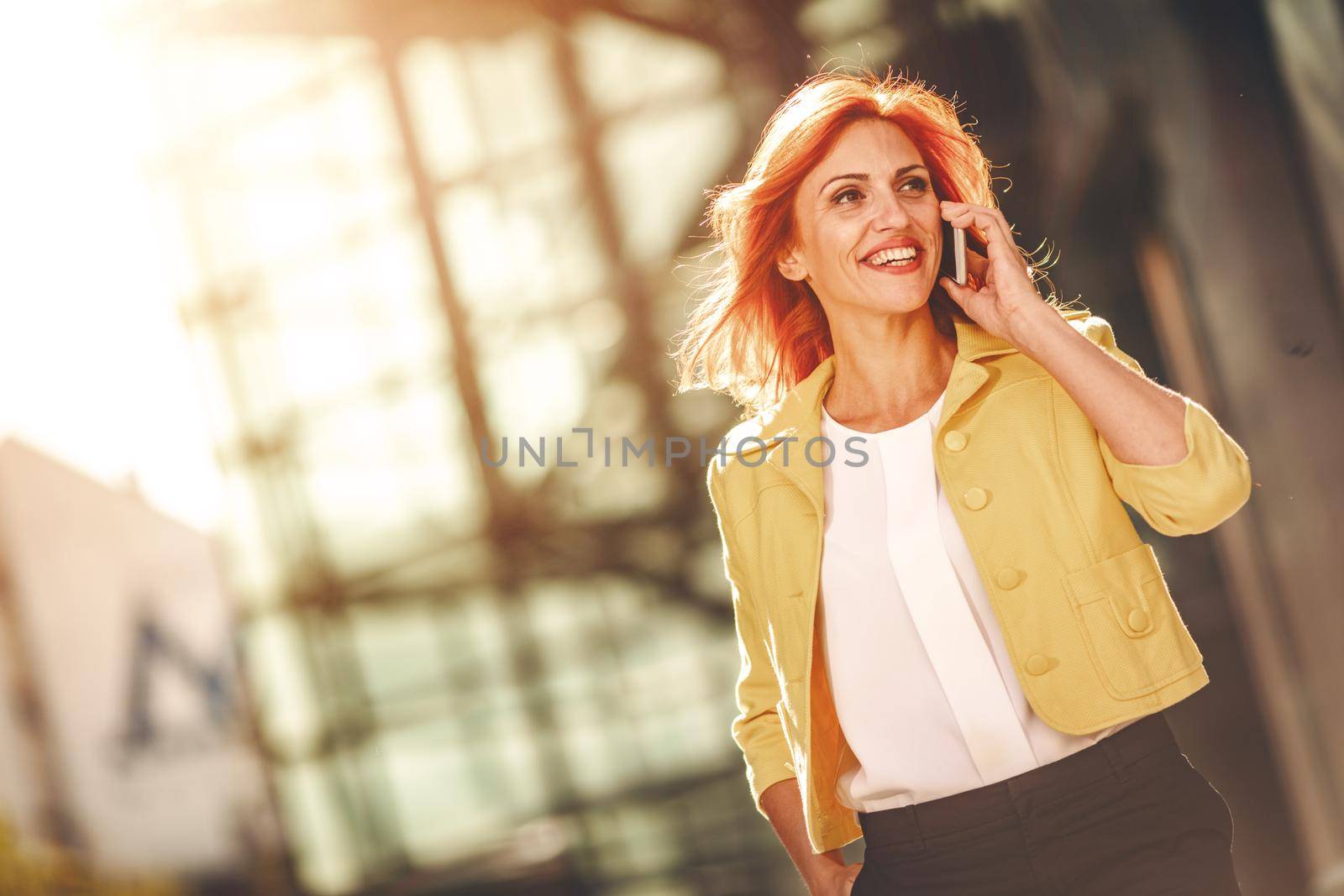 Smiling successful business woman is talking on smartphone in office district.