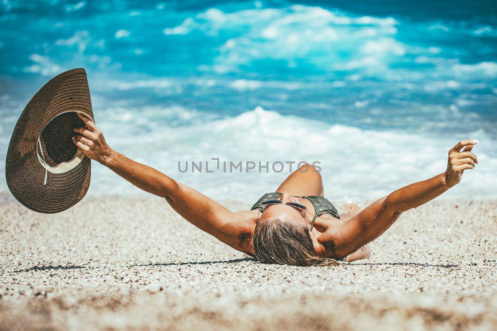 A young woman relaxing on the beach. She is lounging and sunbathing on the coast in the sea.