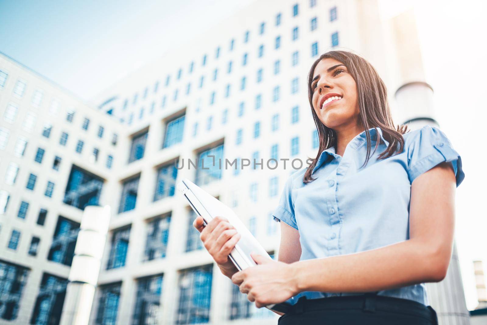 Emotional portrait of a happy and beautiful young businesswoman who carries a laptop on the background of a business center.