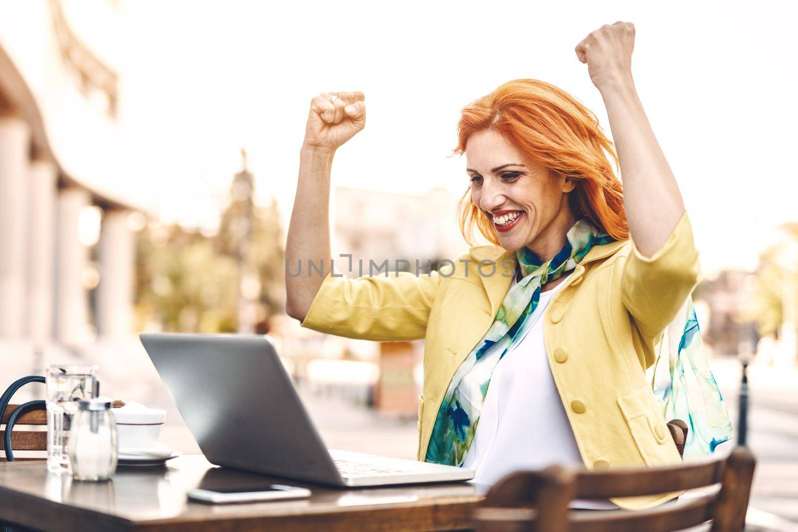 Successful business woman received good news using laptop on a coffee break in a street cafe.