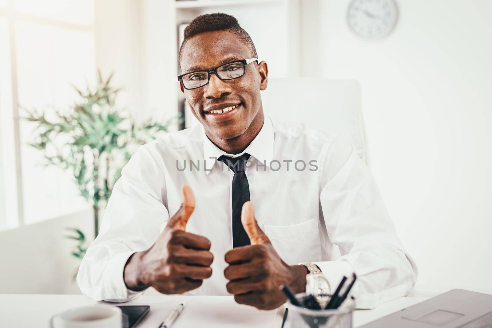 African businessman is sitting in the office, satisfied with success and shows thumbs up.