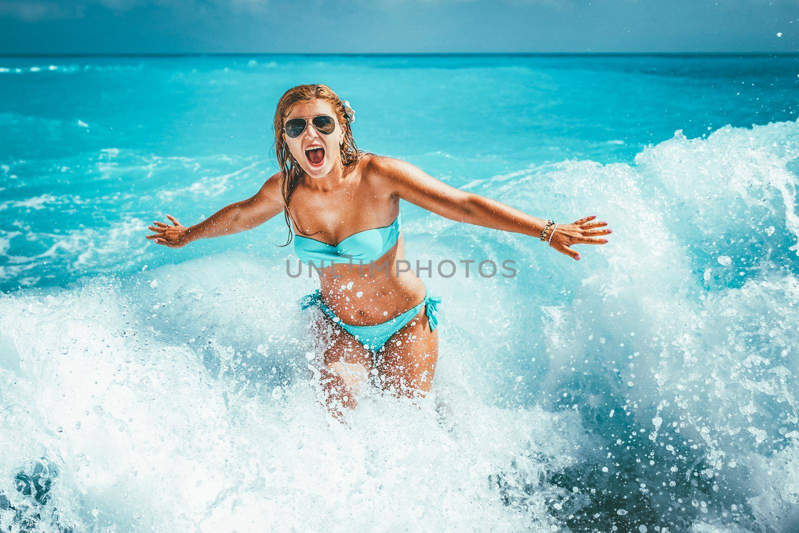 A young woman having fun in the waves of the sea which are splashing her.
