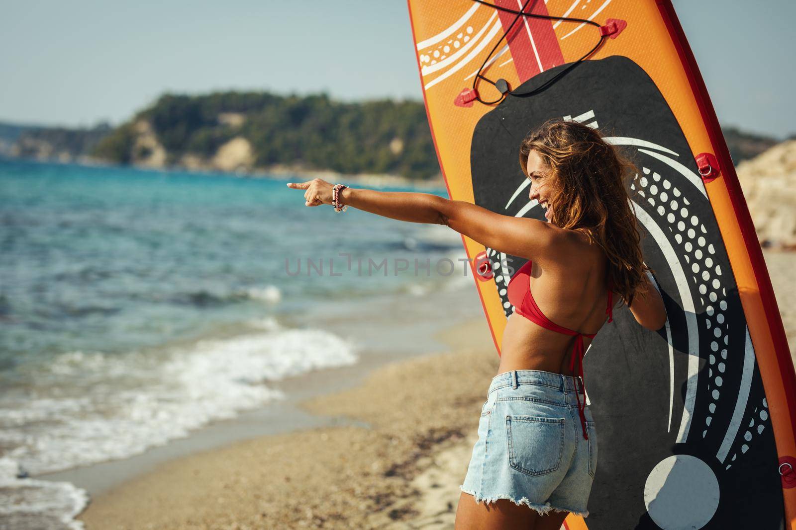 A young woman on a sea beach with a surfboard is ready for the waves.