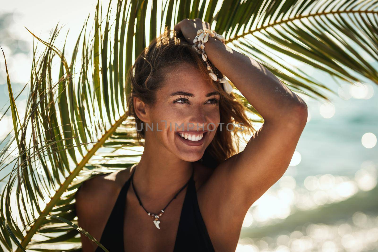 Portrait of an attractive young woman is posing and enjoying at the tropical beach under palm tree leaf.