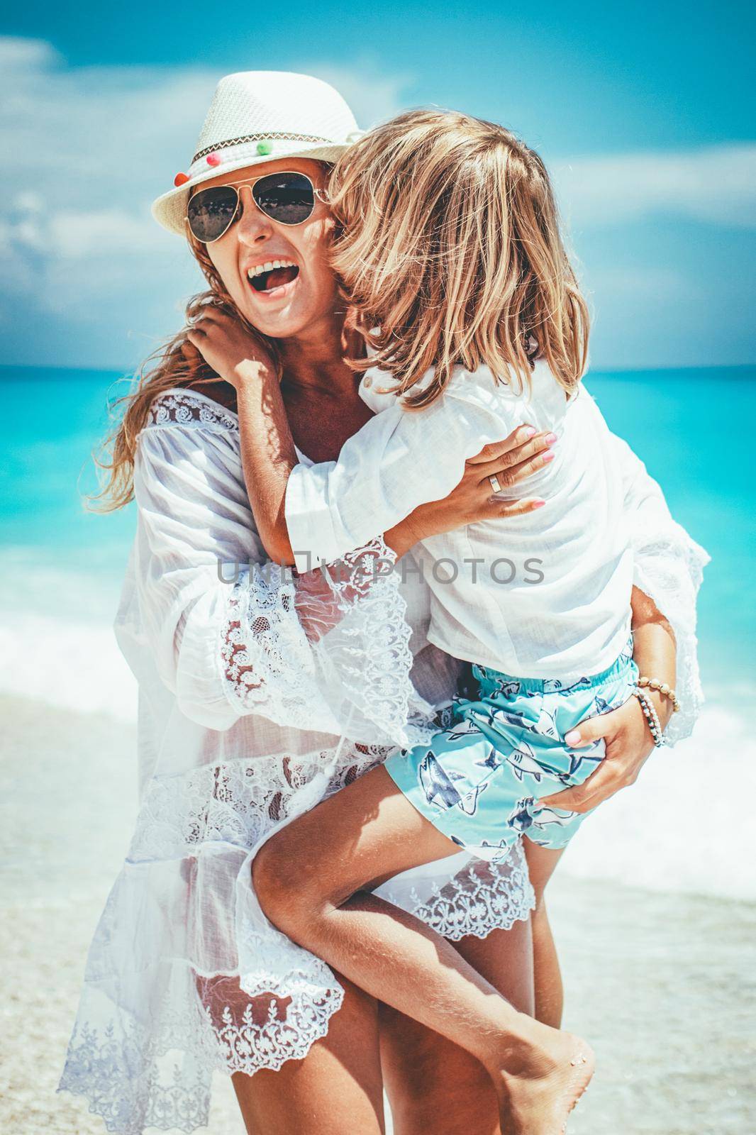 Beautiful little boy enjoying with his mother on the beach. She is embracing him and he is kissing mother's cheek.
