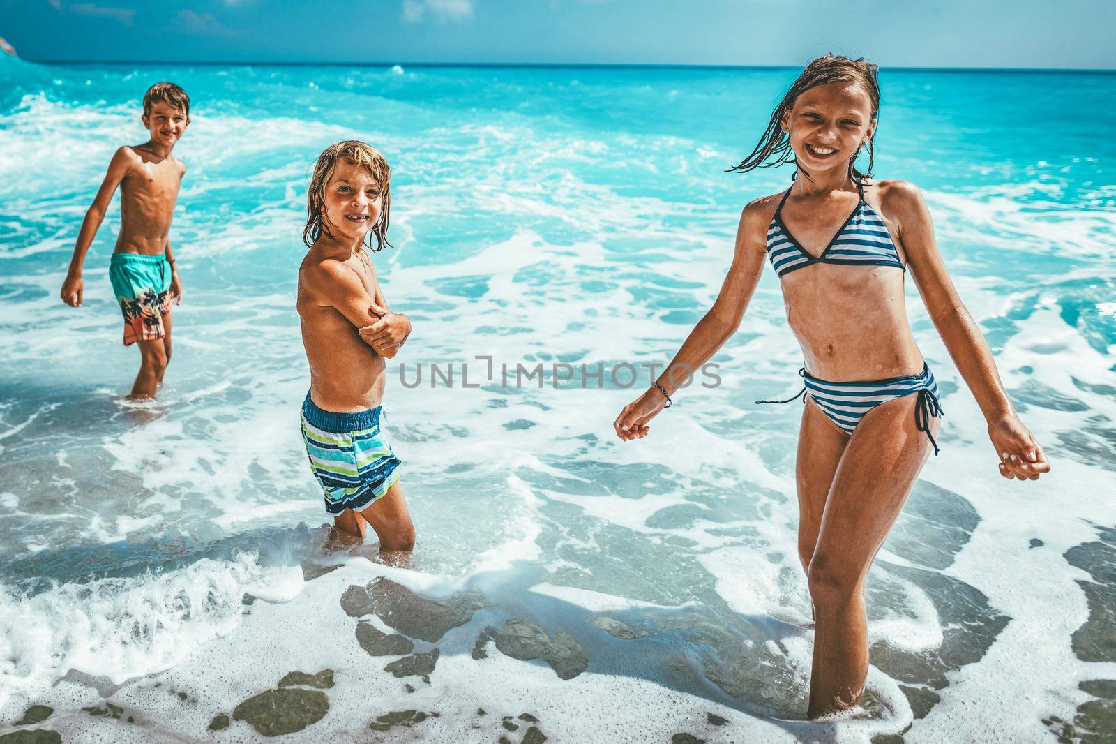 Brothers and sister playing in the shore on the beach during the hot summer vacation day.