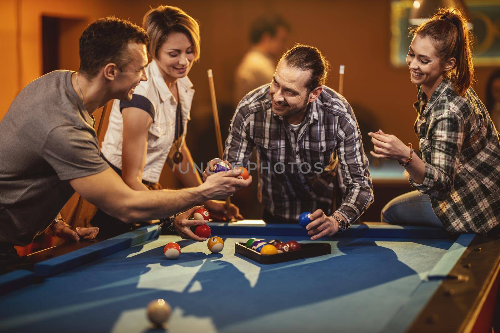 Young cheerful friends are playing billiards in bar after work. A couple that wins fame and the losers are in a bad mood.