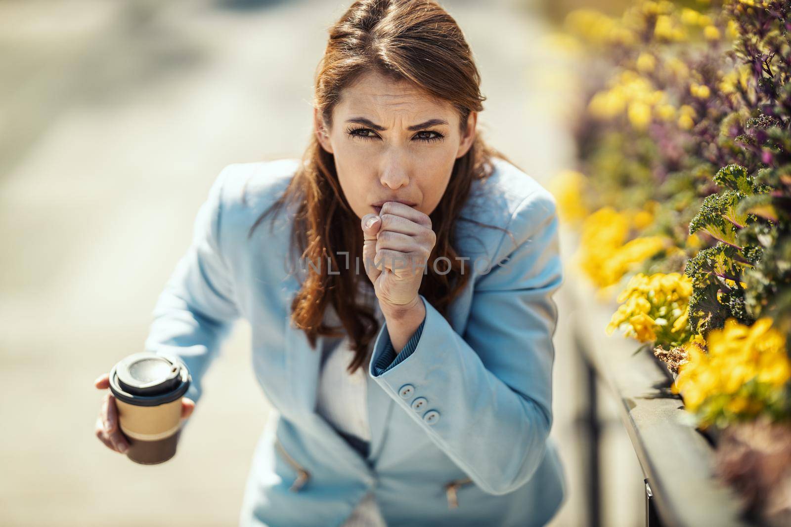 Young businesswoman on coffee break outside coughing due to allergies or colds.