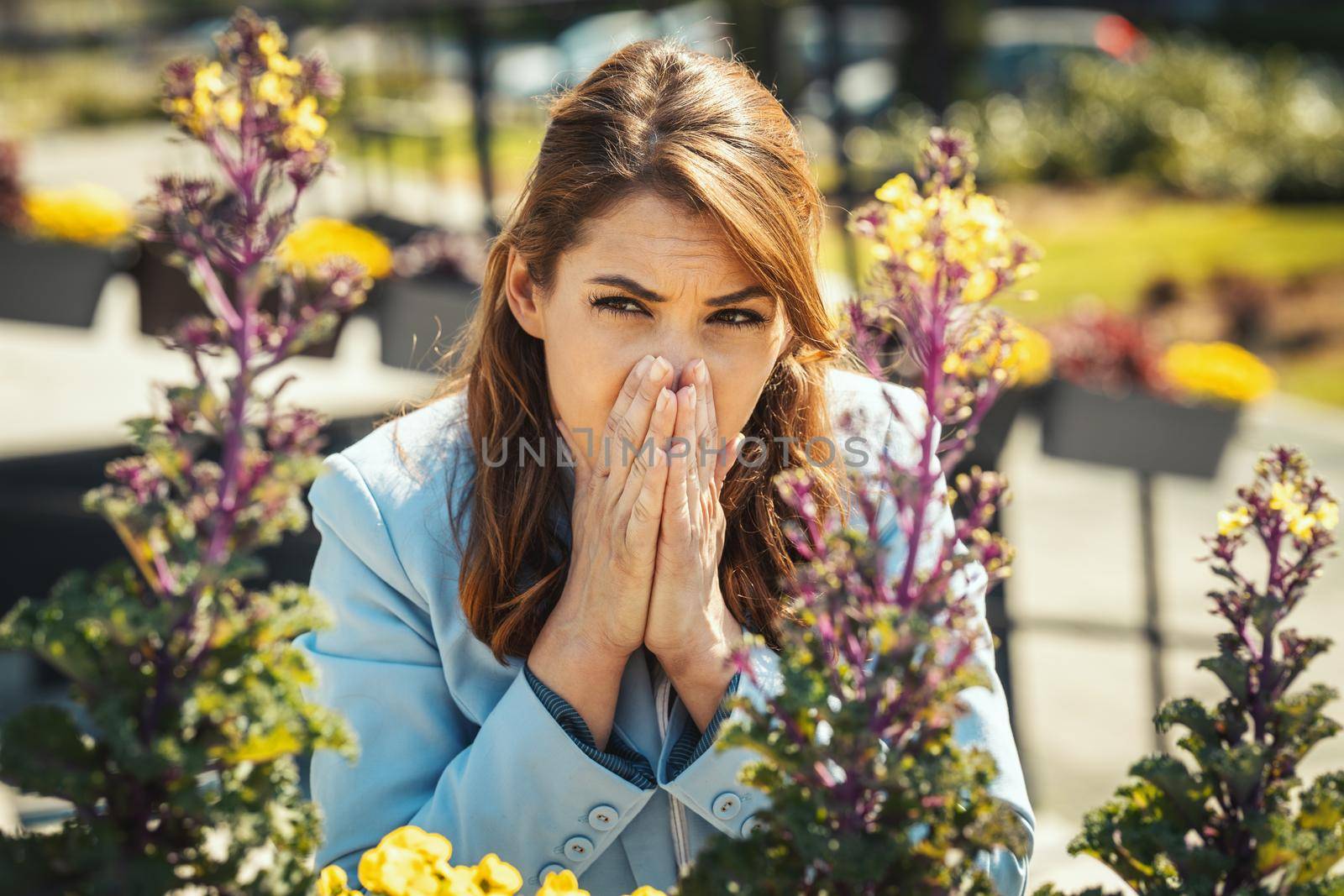 Young businesswoman on break outside sneezing due to allergies or colds.
