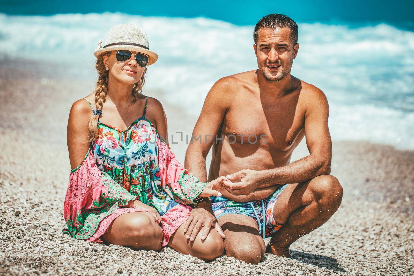 Young man and woman are posing on the sea beach in summer day and looking at camera.