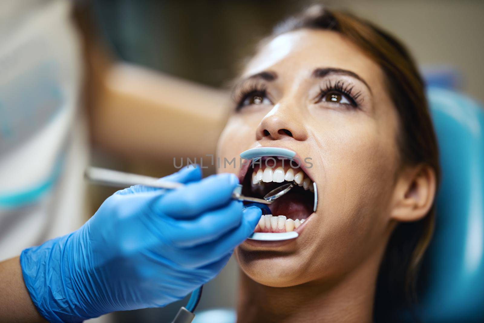 The beautiful young woman is at the dentist. She sits in the dentist's chair and the dentist sets braces on her teeth putting aesthetic self-aligning lingual locks.