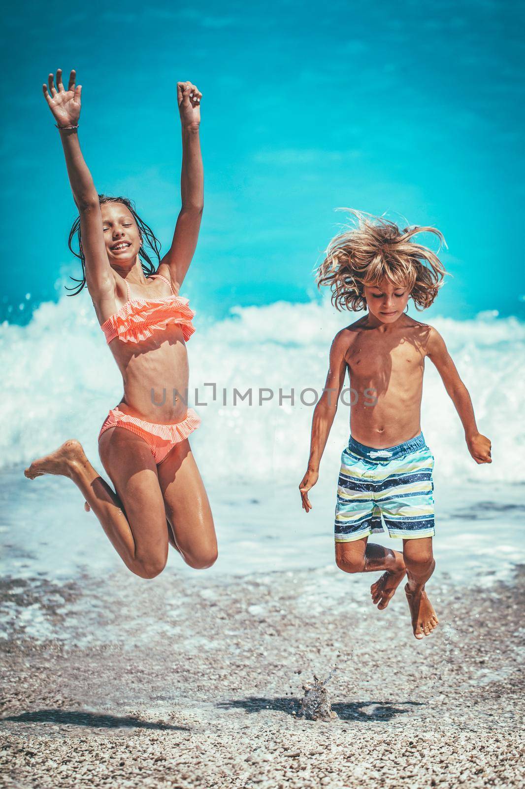 Brother and sister are playing and having fun in the shore on the beach during the hot summer vacation day. They are enjoying and jumping on the beach.