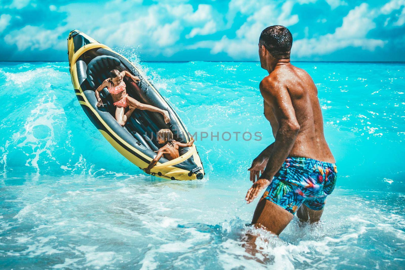 Happy family is enjoying floating in yellow kayak at tropical ocean water during summer vacation. The father is guarding children who are driving in a rubber boat and waves are splashing them.