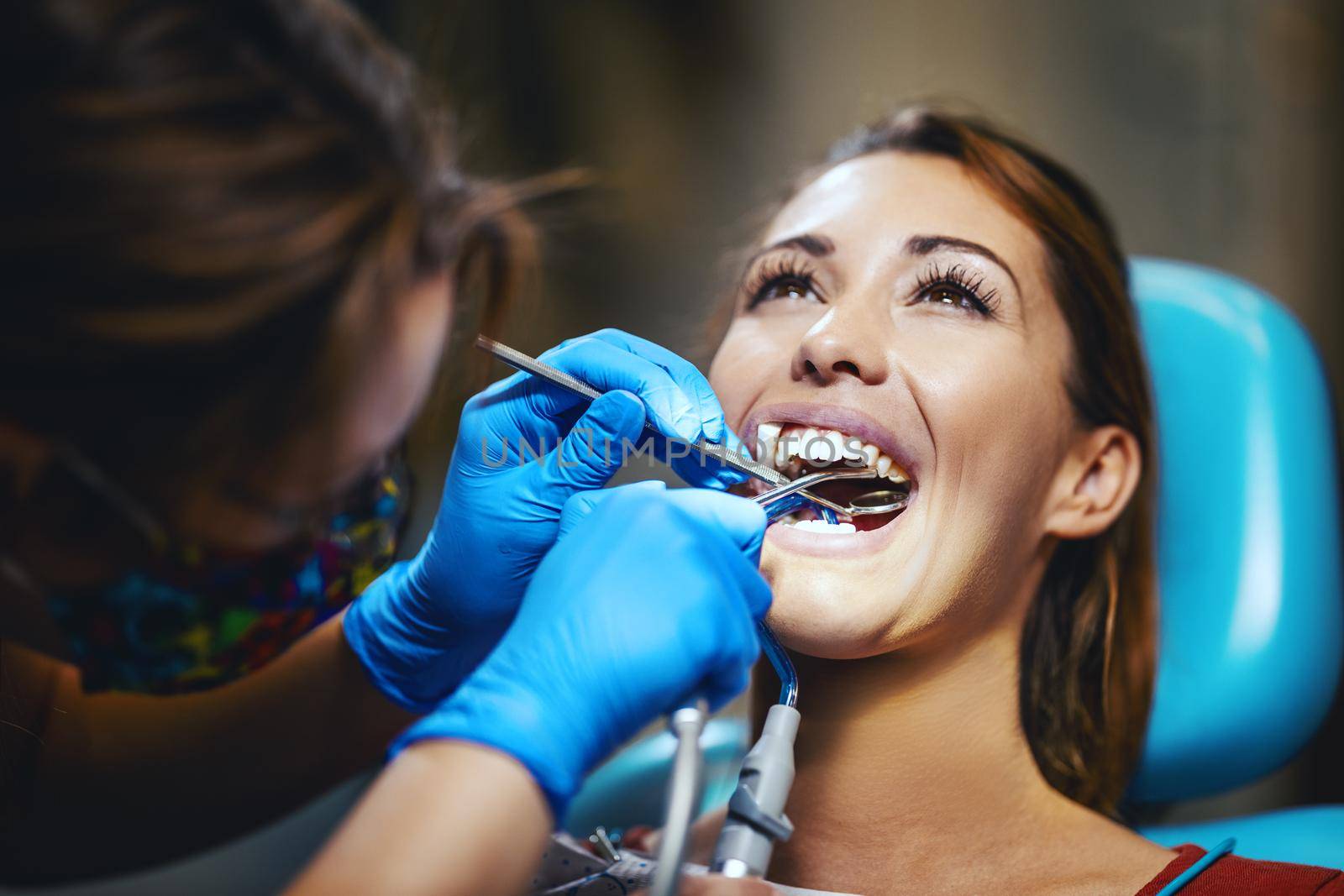 The beautiful young woman is at the dentist. She sits in the dentist's chair and the dentist sets braces on her teeth putting aesthetic self-aligning lingual locks.