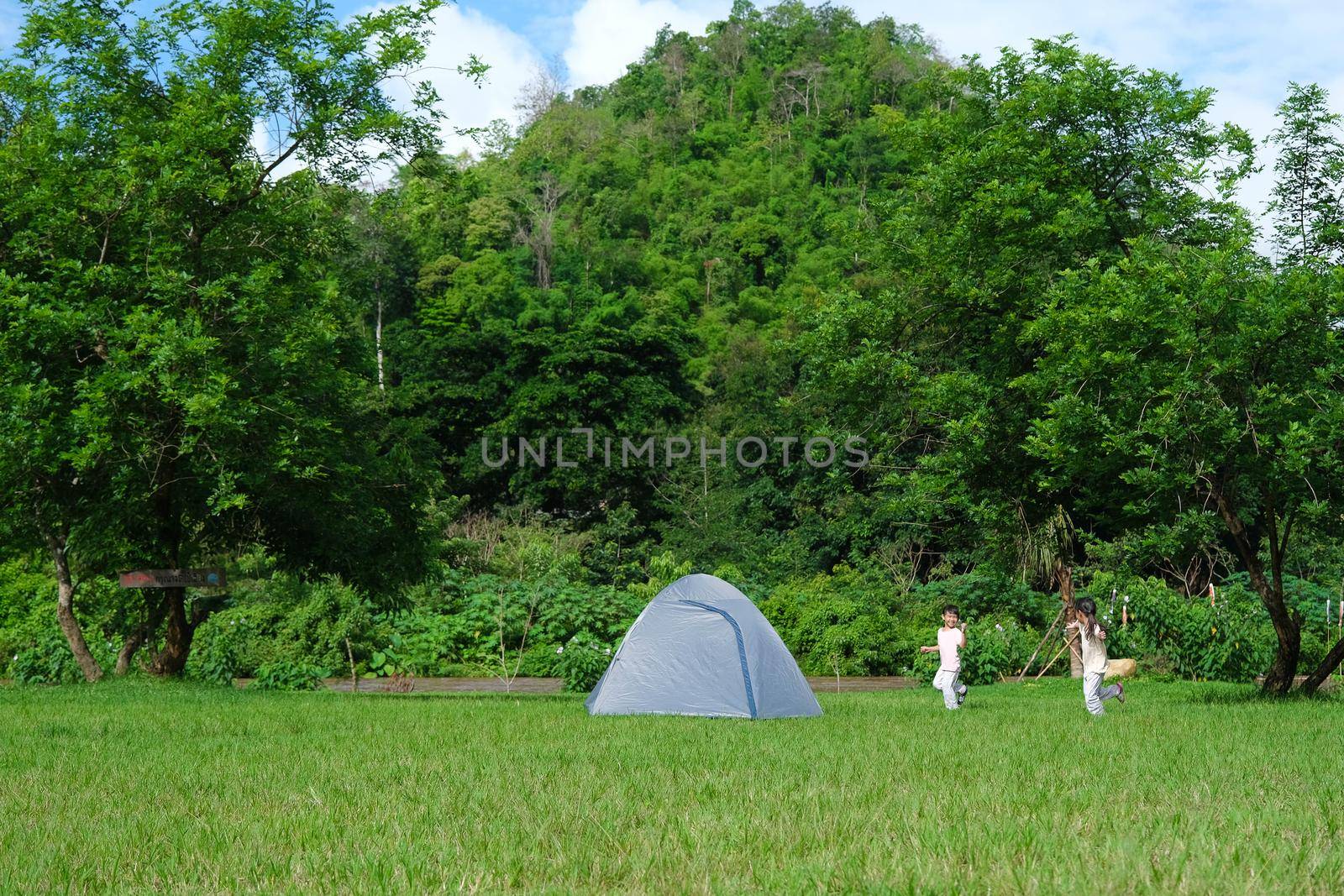 Happy little sisters play together in a campsite during summer vacation in the countryside. Two cute little girls having fun playing outdoors on a hot summer day. Happy childhood concept.