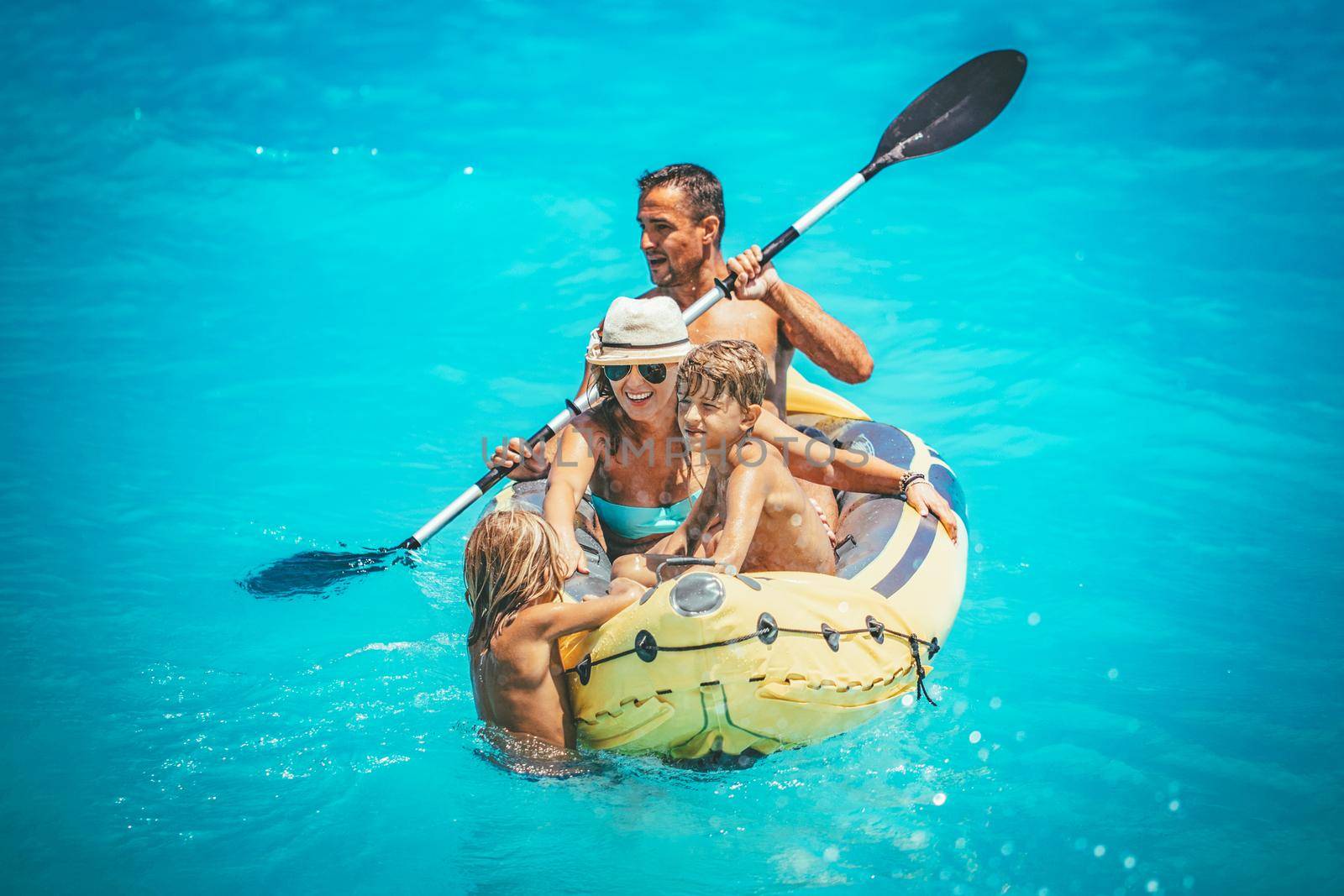 Happy family is enjoying paddling in yellow kayak at tropical ocean water during summer vacation.They are kayaking on the sea.