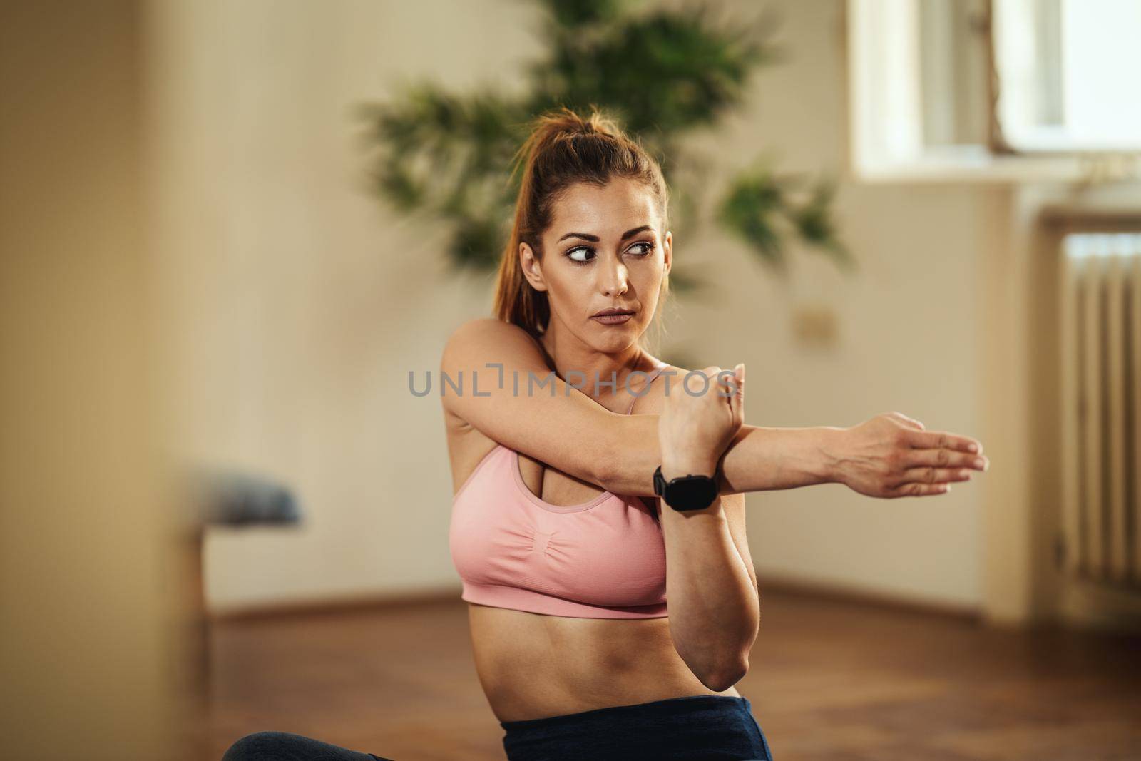 Young smiling woman is doing stretching exercises at home in morning sunshine.