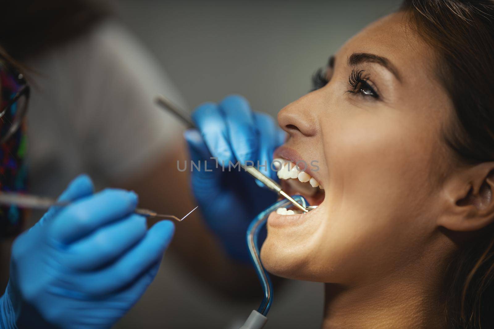 The beautiful young woman is at the dentist. She sits in the dentist's chair and the dentist sets braces on her teeth putting aesthetic self-aligning lingual locks.