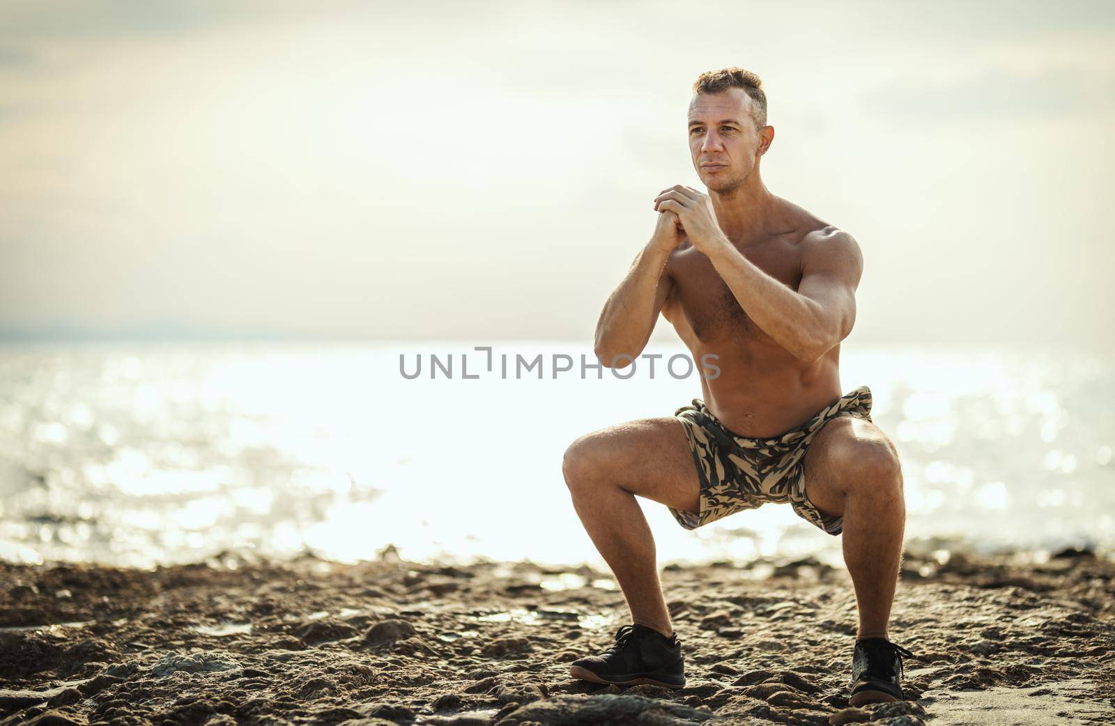 A handsome man ais doing stretching exercise at the sea beach in summer sunny day.