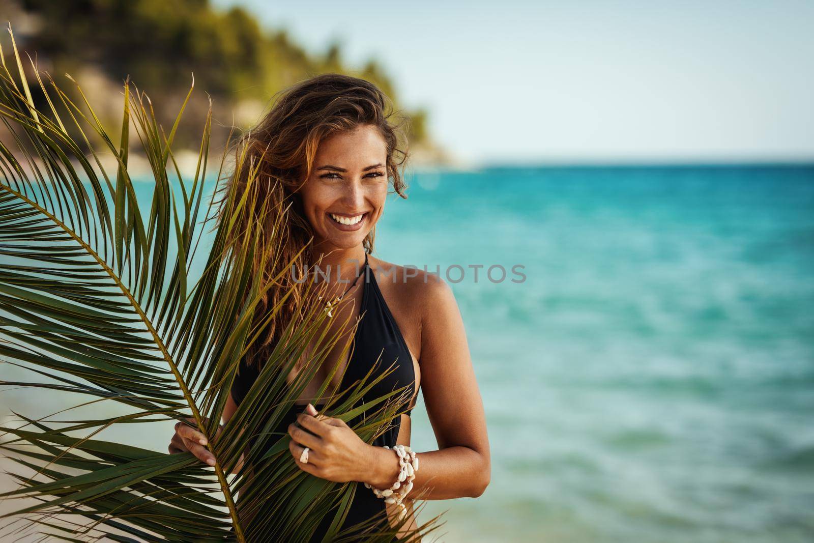 Shot of an attractive young woman is posing and enjoying covered with palm tree leaf at the tropical beach.