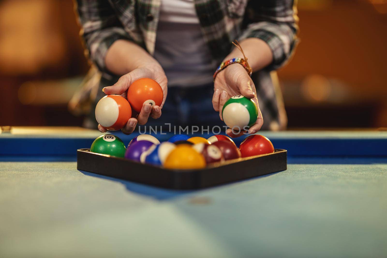 Close-up of a young woman's hands places billiard balls on a pool table to play.