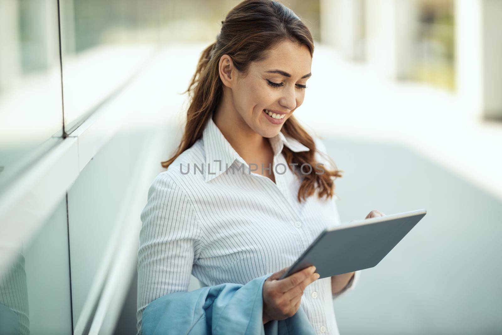Young smiling businesswoman is surfing social network on digital tablet in front of office during break.