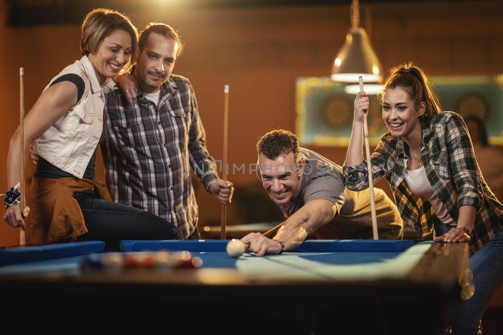 Young cheerful friends are playing billiards in bar after work. A couple that wins fame and the losers are in a bad mood.