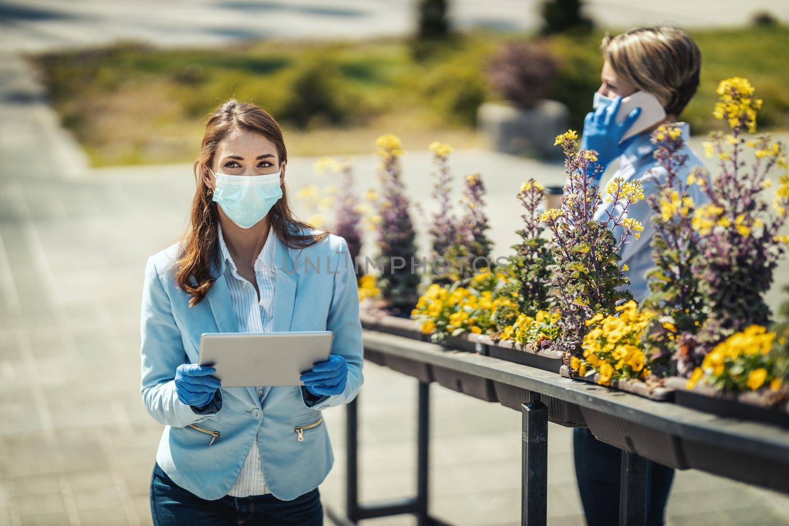 Young business woman with protective mask on her face is looking something on her digital tablet outdoor during COVID 19 pandemic.