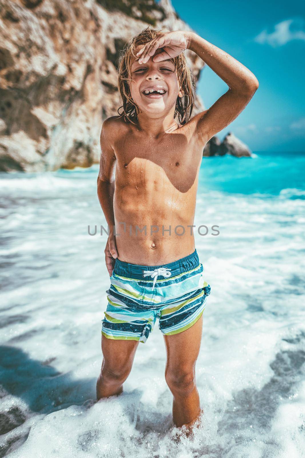 Cute boy enjoying on the beach standing in the sea waves. 
