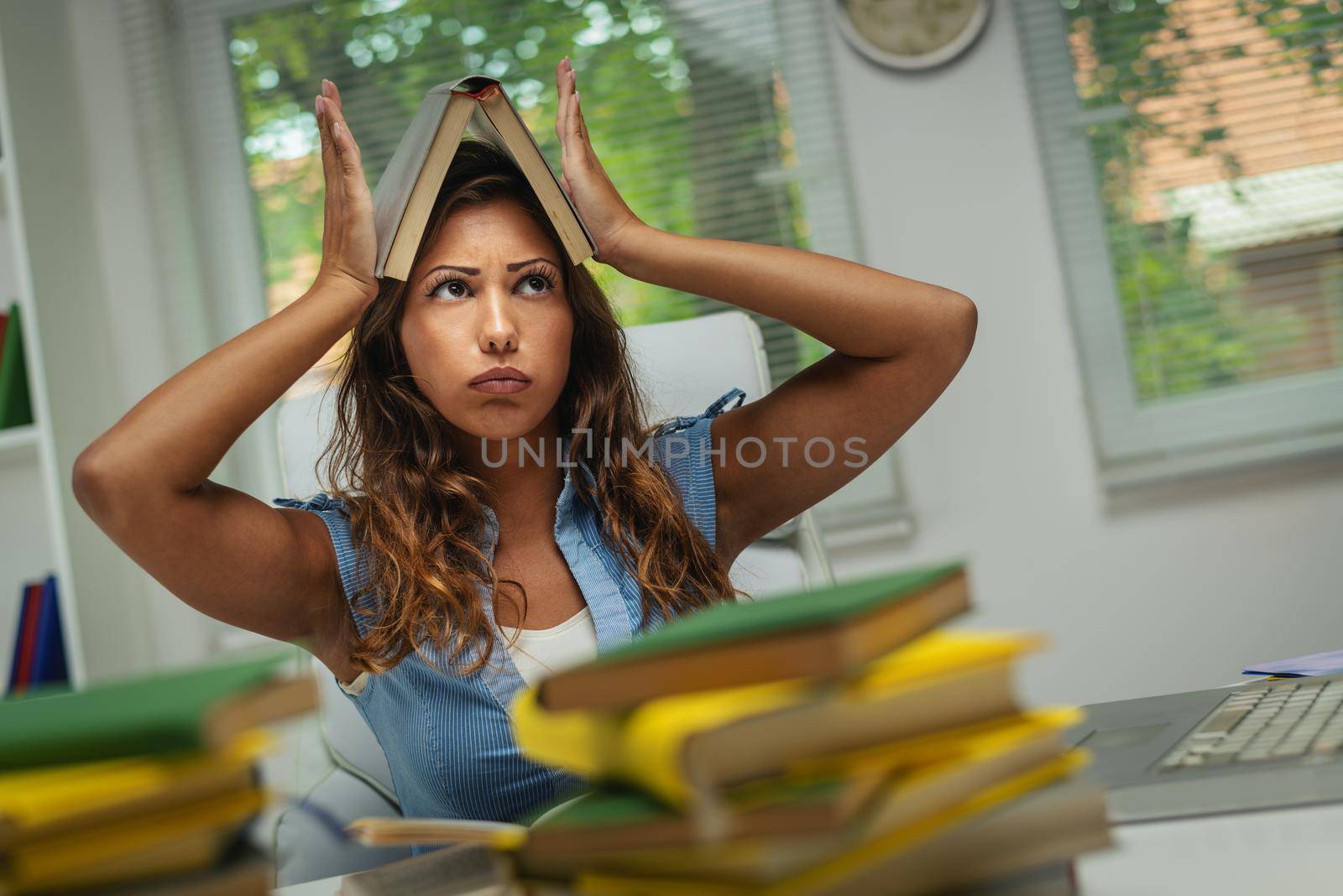 A beautiful bored young female student  with book is preparing exam and learning lessons in school library.
