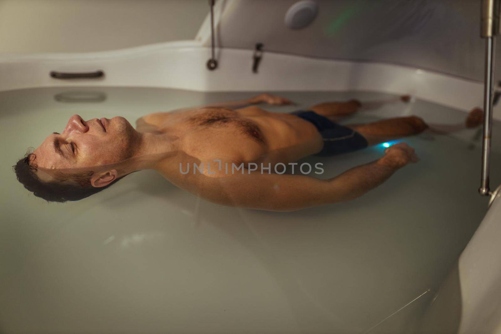 Relaxed man is floating in a sensory deprivation tank. He is very relaxed. Wellness and Spa concept.