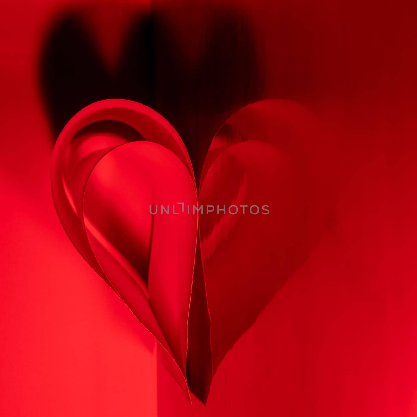 Designer abstract heart made of red paper with reflection on a glossy surface and contrasting shadow.