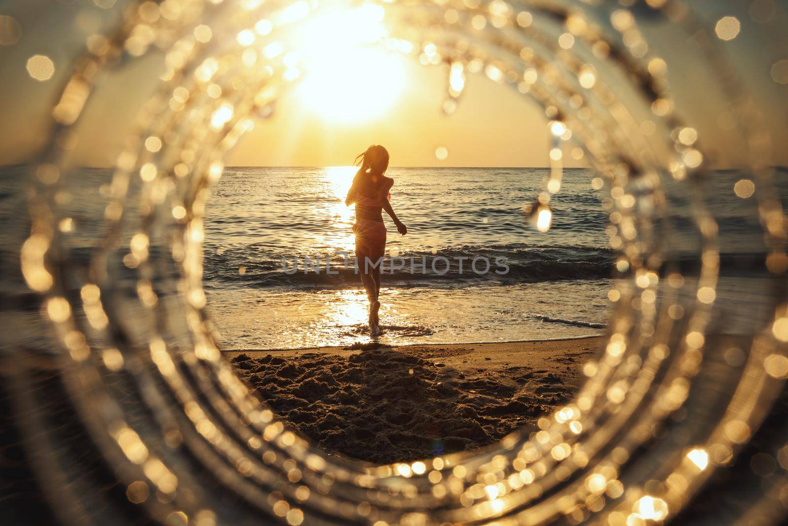 A beautiful creative composition of a beach landscape shot through a circle focus showing a teenage girl who runs out of the sea in sunset.