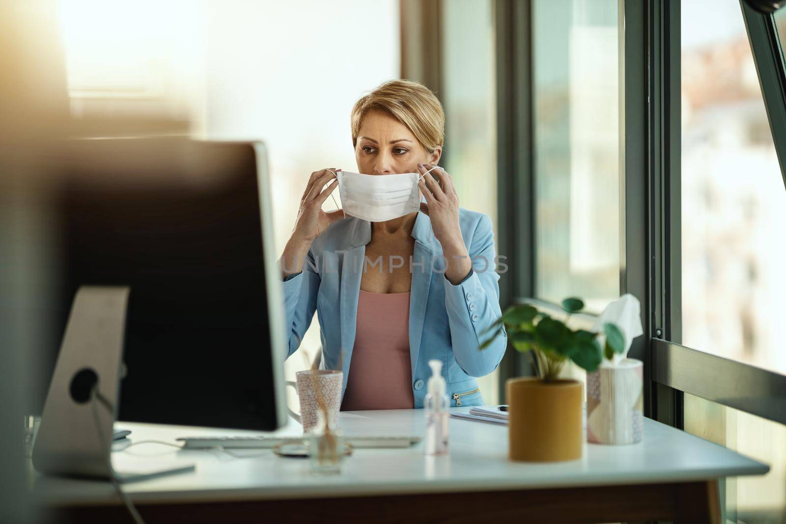 Business woman in a medical protective mask works at the office on the computer during self-isolation and quarantine to avoid infection during flu virus outbreak and coronavirus epidemic.