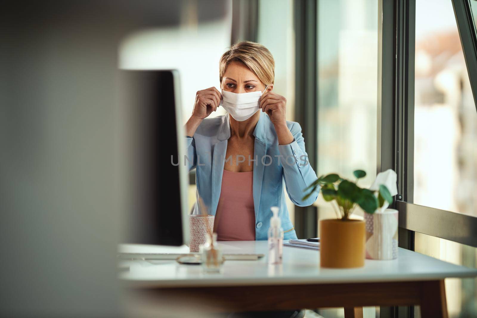 Business woman in a medical protective mask works at the office on the computer during self-isolation and quarantine to avoid infection during flu virus outbreak and coronavirus epidemic.